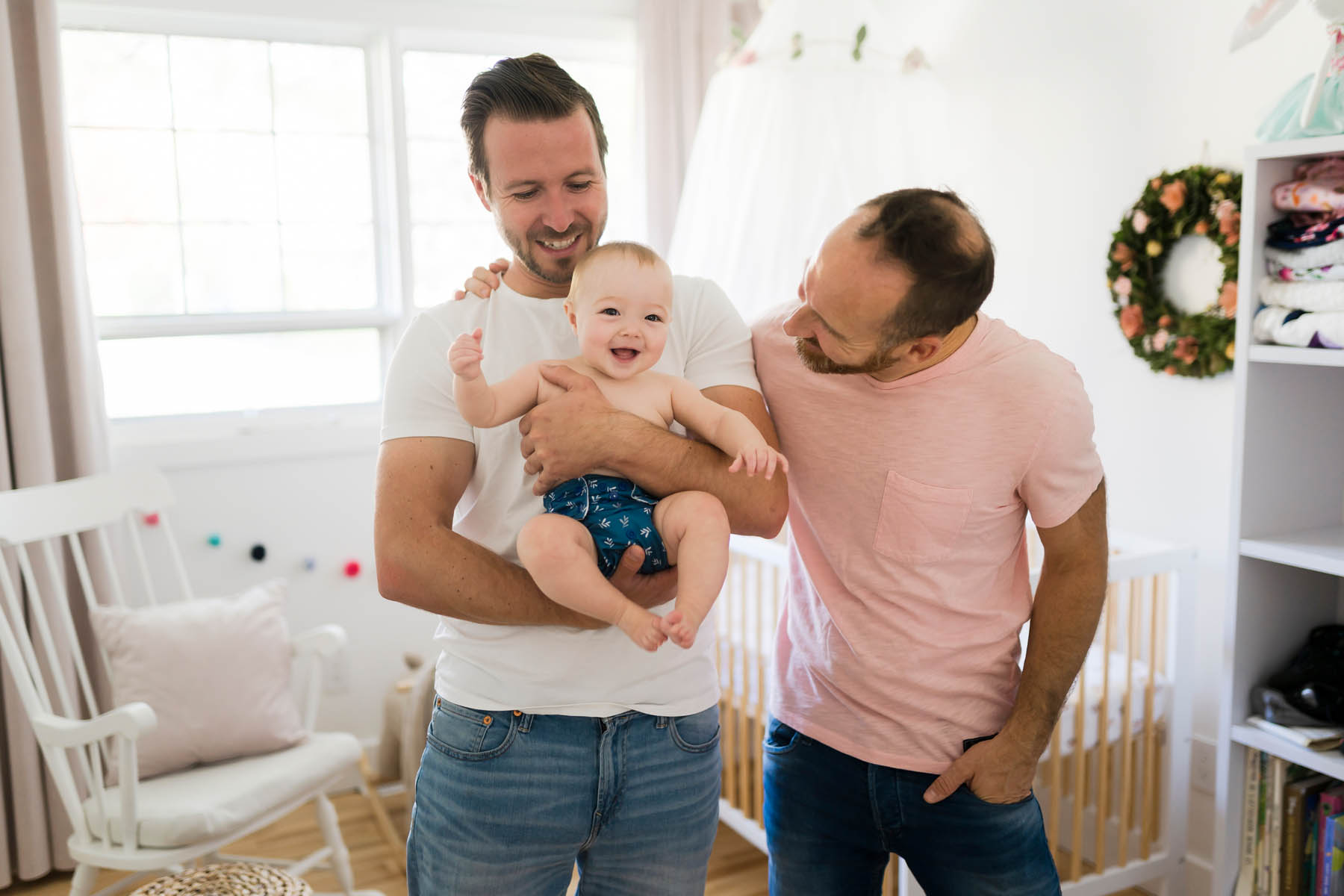 Male gay parents relaxing in baby room holding it