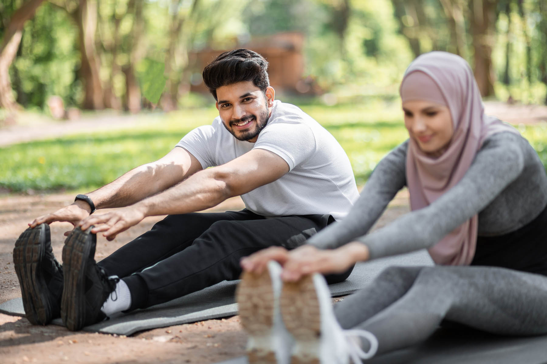 Arabian man and woman in hijab warming up on yoga mat before outdoors workout