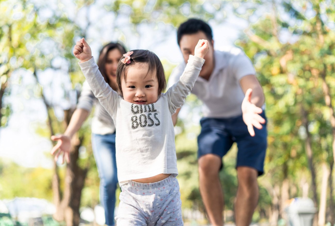 happy little Asian toddler girl running in park with parents