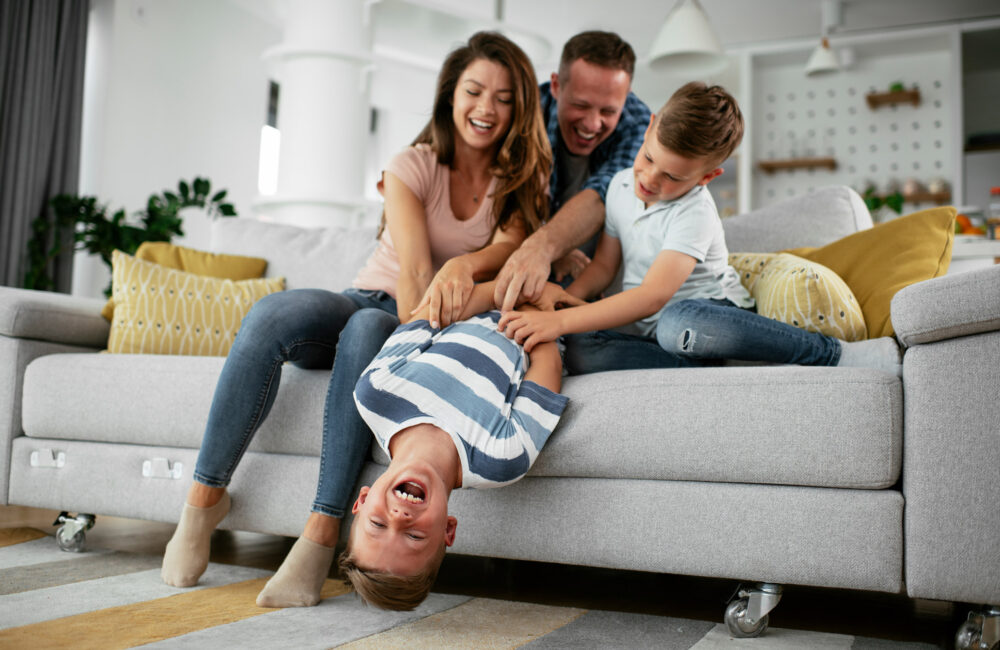 two parent and a brother tickle another son on a couch