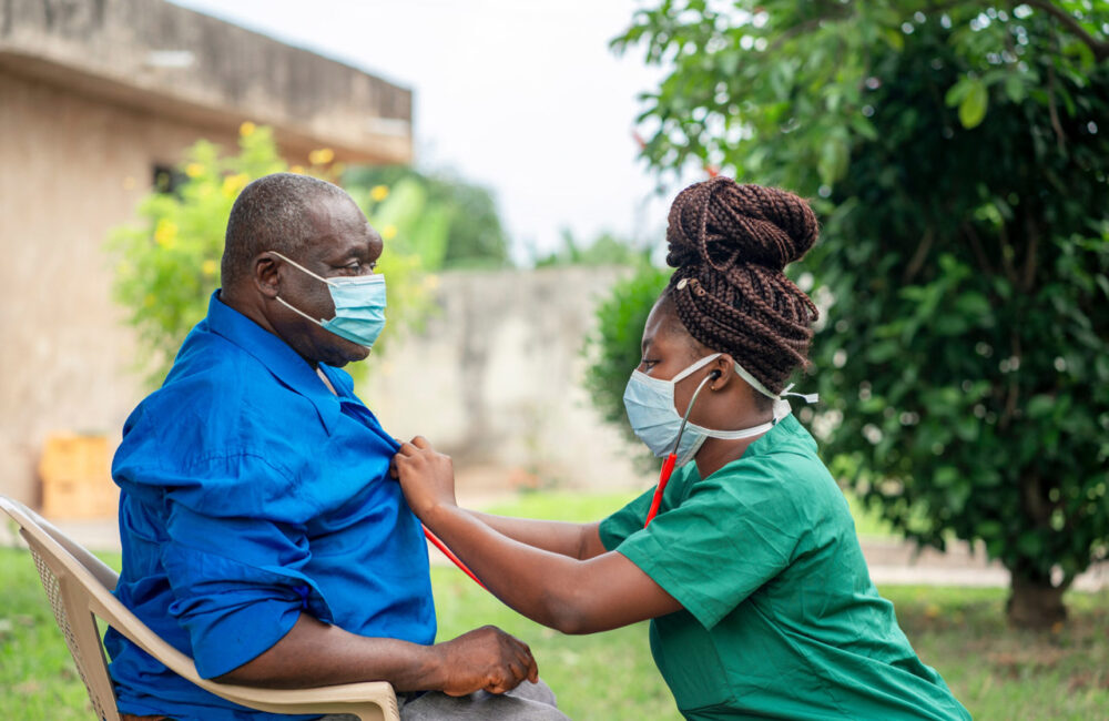 young black nurse wearing a face mask taking care of an old man